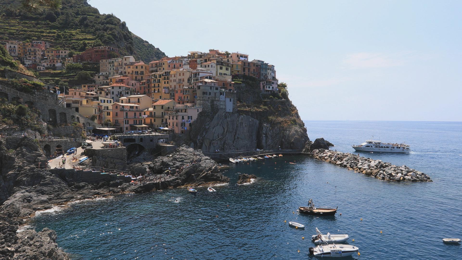 "Die Italienische Riviera": Ein Bergdorf der Cinque Terre mit Meer und Booten im Vordergrund.