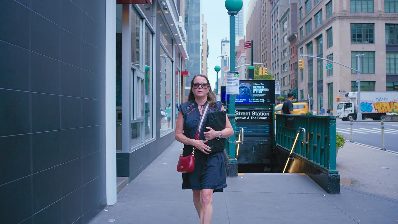 Eine Frau mit Laptoptasche, roter Handtasche und Sonnenbrille kommt aus Metro-Station.
