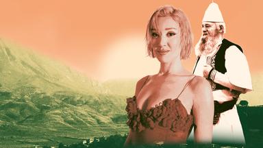 Porträt einer jungen Frau im roten Trägerkleid und einem alten Mann in weißer Tracht und spitzem weißen Hut.