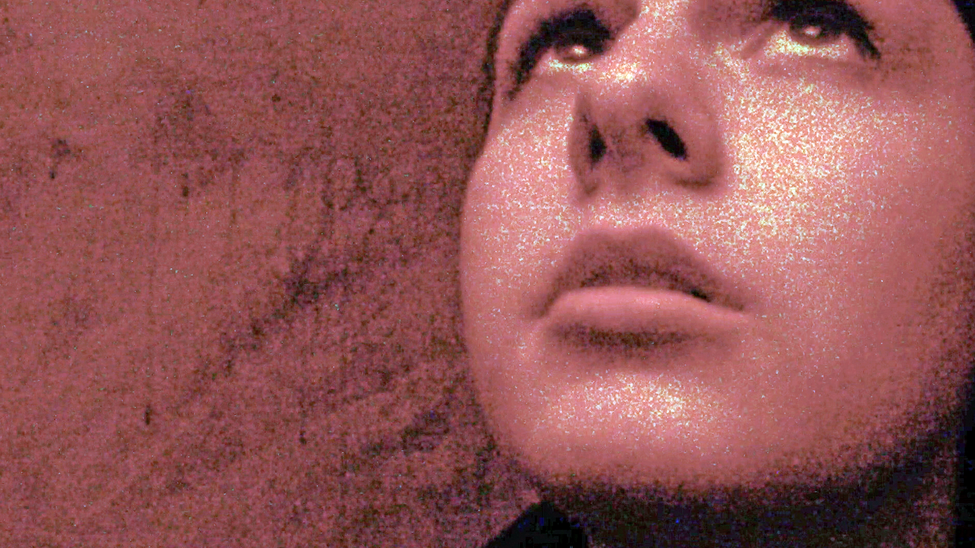 Nahaufnahme einer jungen Frau, die nach oben blickt. Das Foto ist stark gekörnt und wirkt künstlerisch verfremdet.
