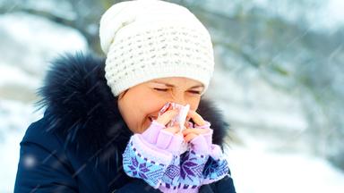 Eine warm angezogene Frau putzt sich im Schneegestöber die Nase