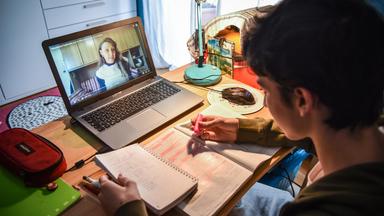 Ein Schüler sitzt vor einem Laptop und macht arbeit online an Schul-Aufgaben