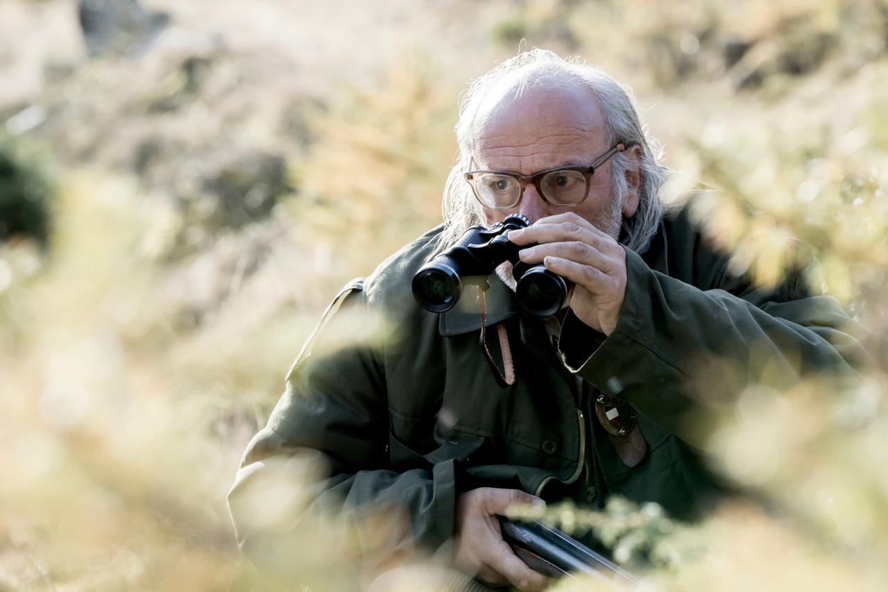 Mann mit Fernglas im Grünen, Gewehr in der Hand