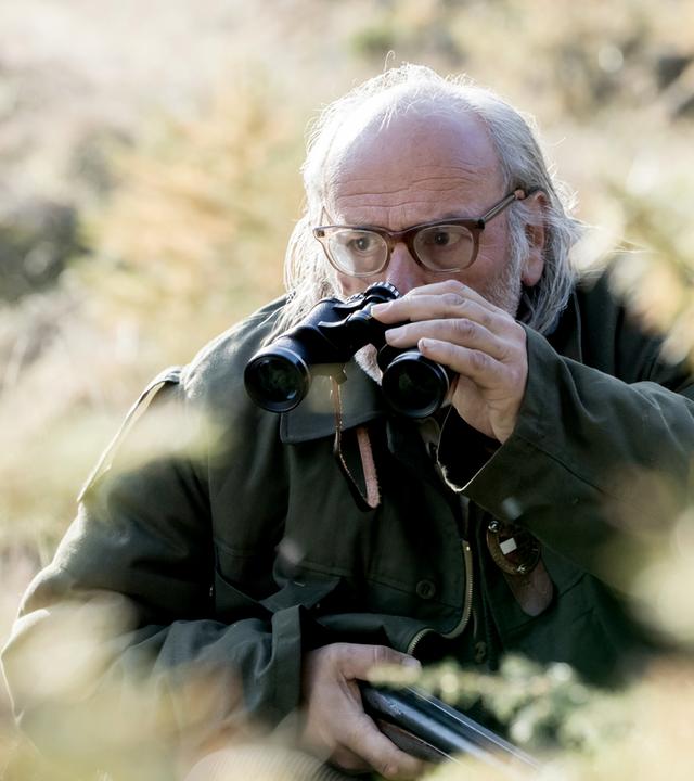 Mann mit Fernglas im Grünen, Gewehr in der Hand
