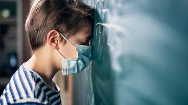 Junge lehnt mit geschlossenen Augen an Schultafel