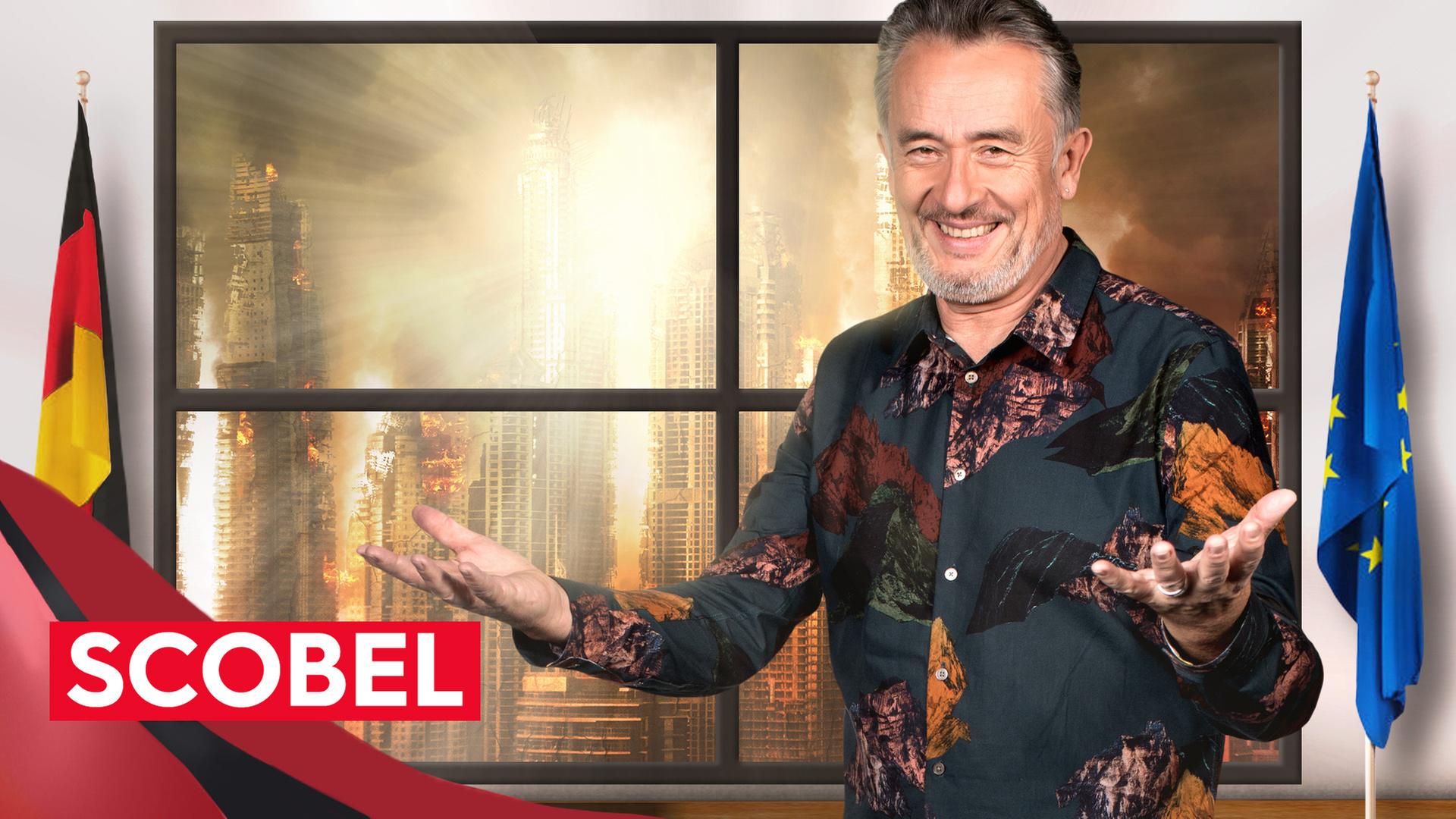 Gert Scobel steht mit geöffentetn Armen dor einem Fenster, neben ihm eine Europa-Flagge