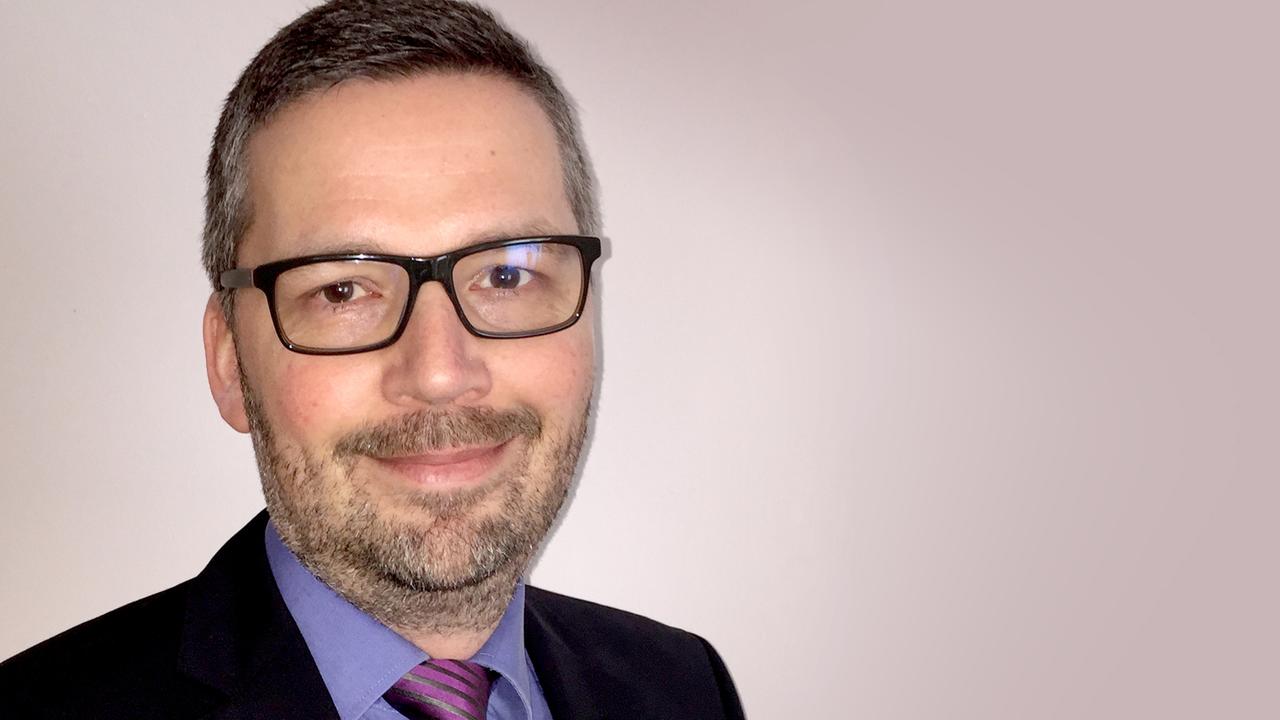 Mikrobiologe Ralf Heermann im Anzug mit Brille vor weißer Wand