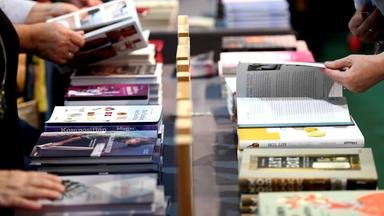 Hände blättern an einem Verlagsstand in aufgereihten Büchern