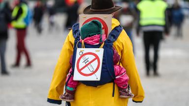 Mann trägt ein Schild auf dem Rücken, um sich als Impfgegner kenntlich zu machen.