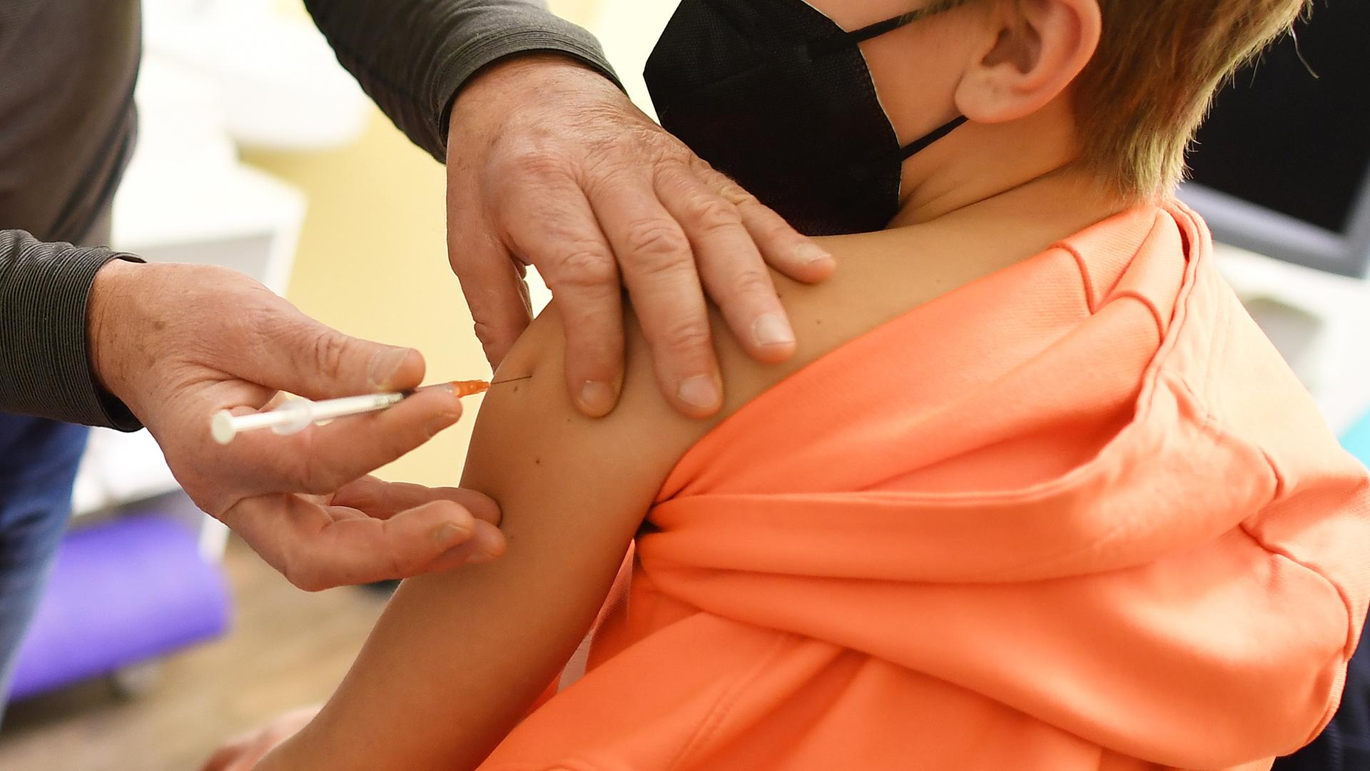 KInd im orangefarbenen Pulli wird geimpft