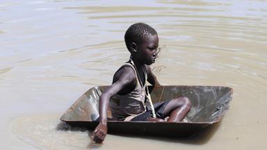 Südsudan: KInd sitzt in einer Schubkarre, von Wasser umgeben