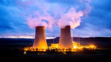 Hell erleuchtetet Atomkraftwerk mit zwei mächtigen Kühltürmen in der Dämmerung