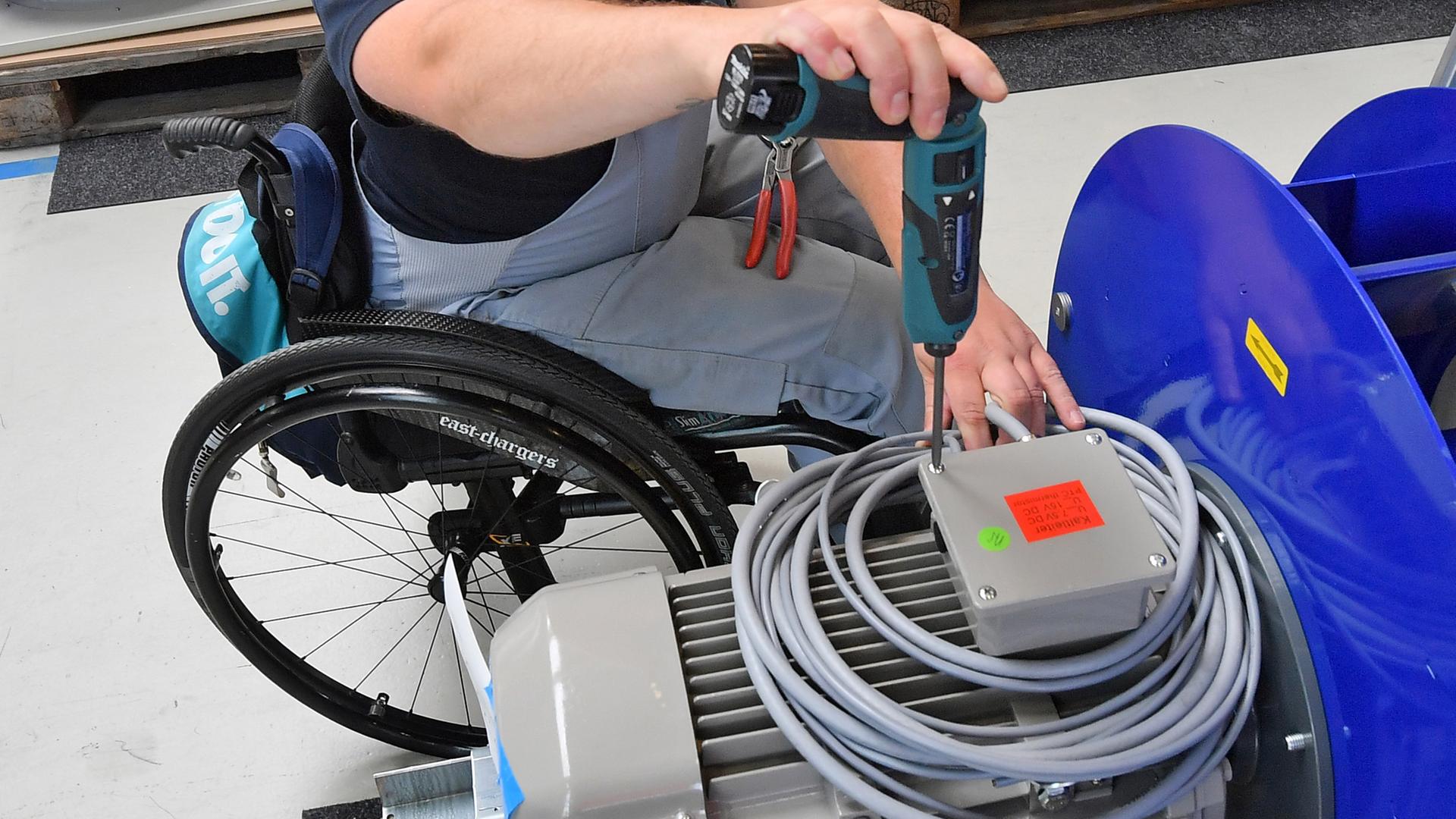 Behinderter in einem Rollstuhl verrichtet Montagearbeiten.