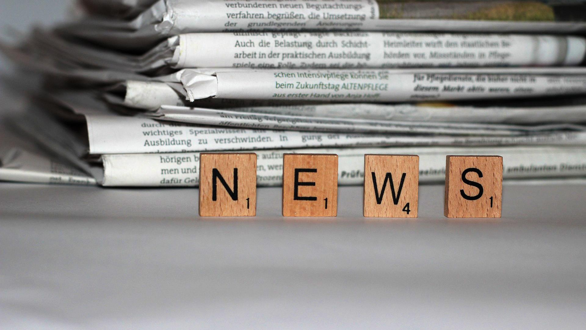 Zeitungstapel, im Vordergrund Spielsteine mit der AUfschrift "News"