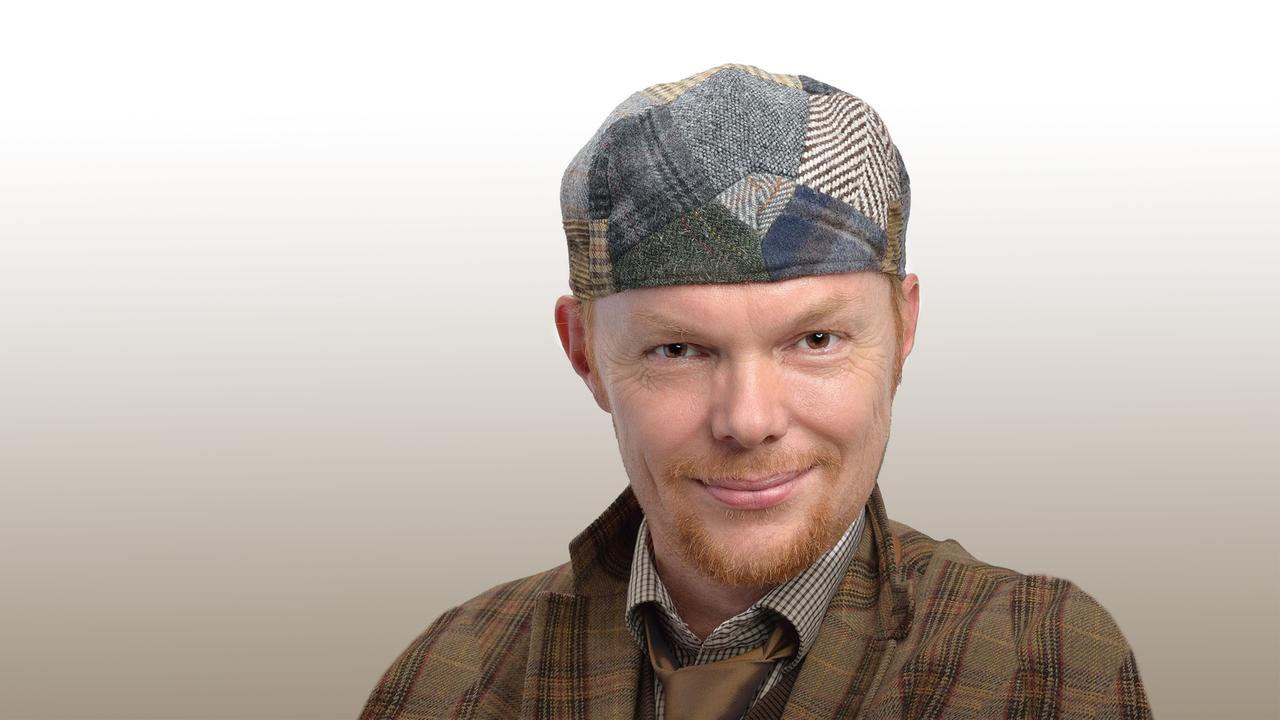 Hektor Haarkötter bedeckt mit seiner bunt gemusterten Schiebermütze sein kurzes rotes Haar. Sein schmunzelndes Lächeln umgib ein kurzer, gepflegter Bart. 