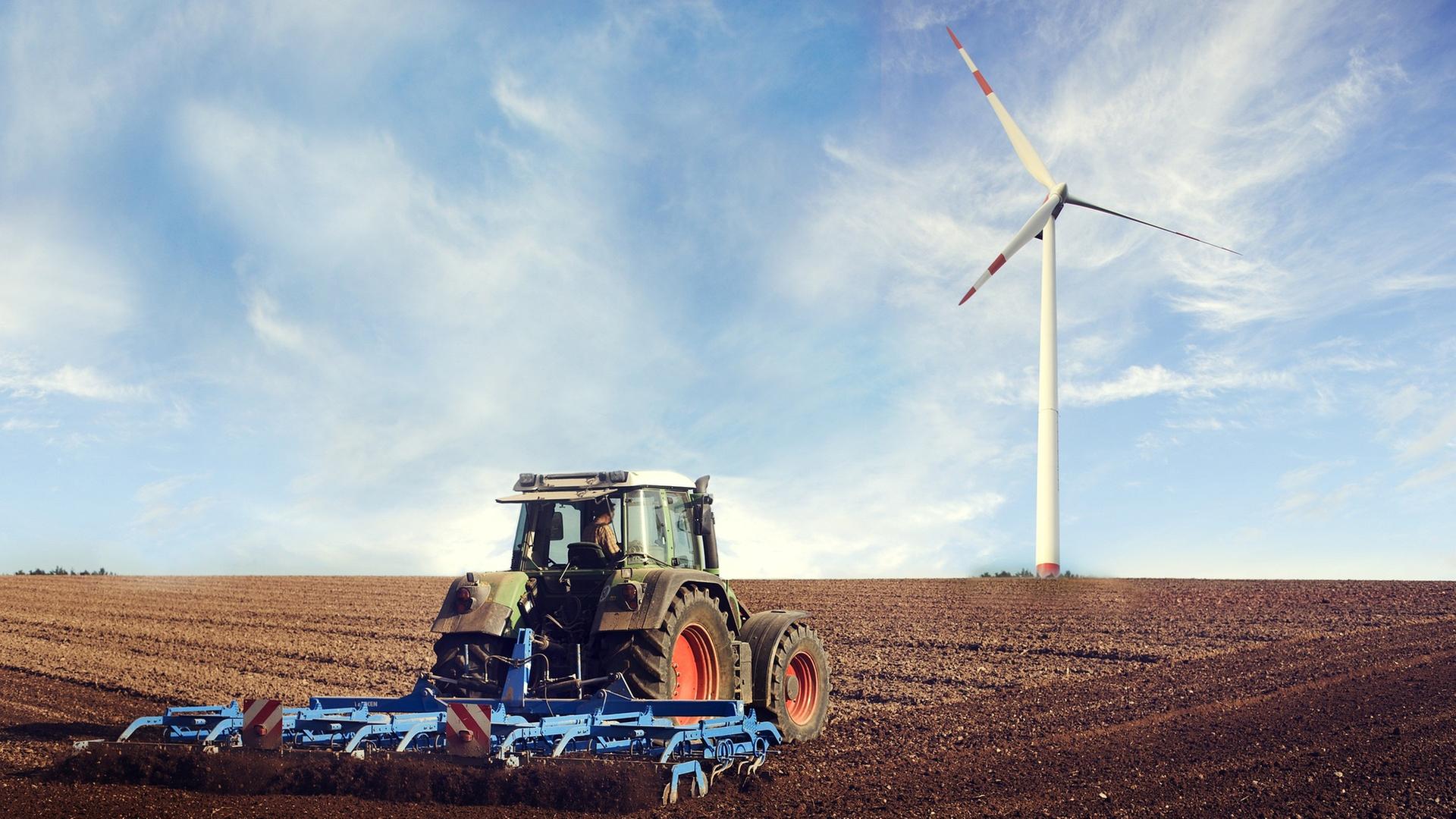 Traktor fährt auf eine Feld, im HIntergrund ein WIndrad
