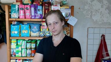 Mann in schwarzem Shirt sitzt vor einem Lebensmittelregal