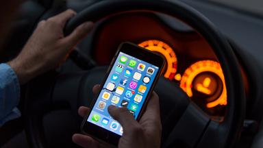 Person amAUtosteuer mit Handy in der Hand