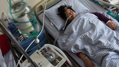 Mensch in Krankenhausbett, angeschlossen an Apparate und Schläuche