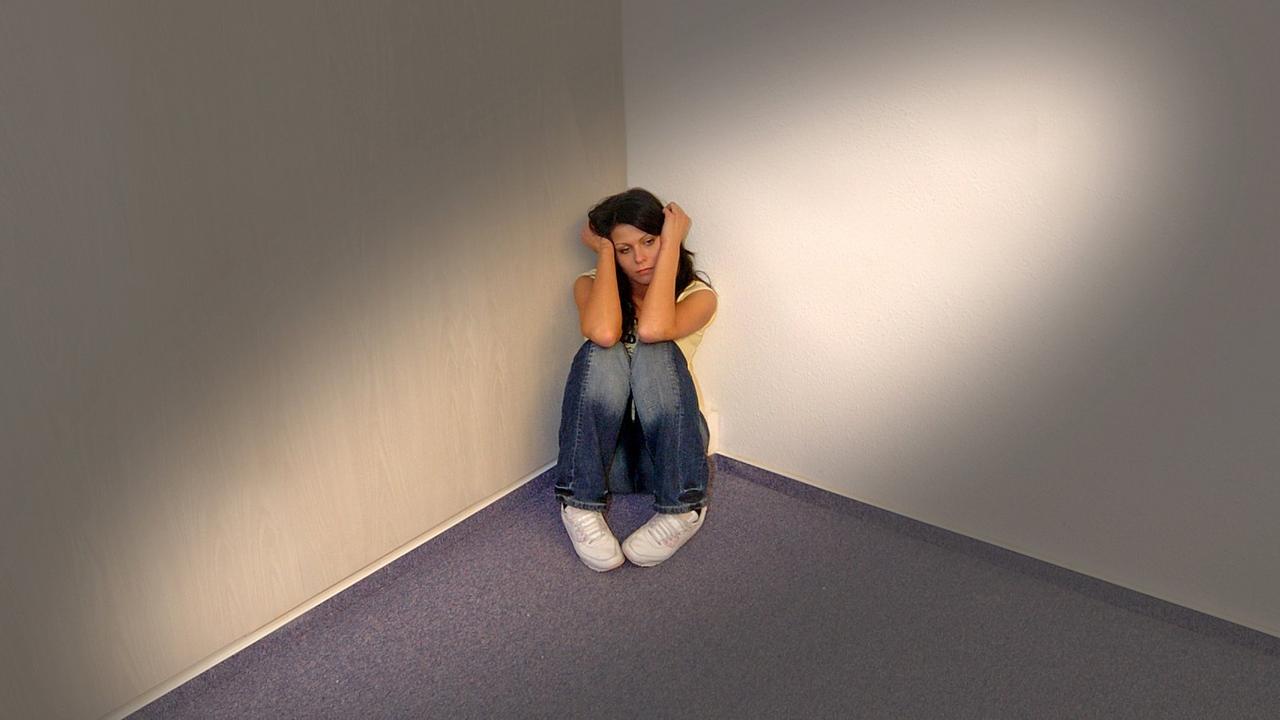 Frau sitzt verängstigt in der Ecke eines Raumes