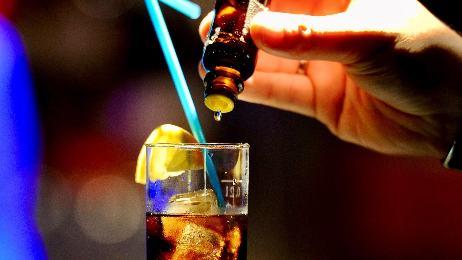 Tropfen werden aus einer kleinen Flasche in ein Glas gegeben