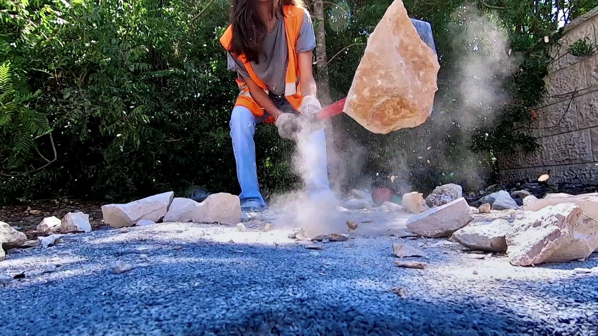 Mädchen - zu sehen im Hintergrund - zertrümmert einen Steinbrocken