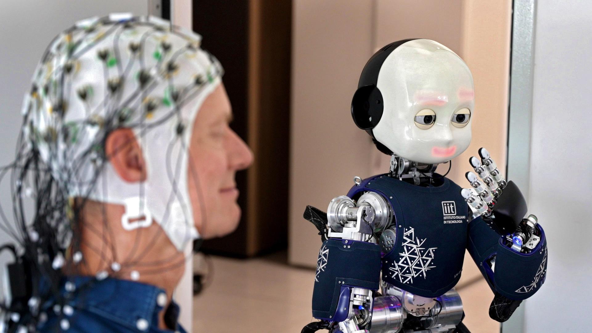 Ingolf Baur mit einer EEG-Haube neben einem humanoiden Roboter