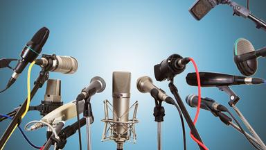 Mehrere MIkrofone in einer Runde vor blauem Hintergrund