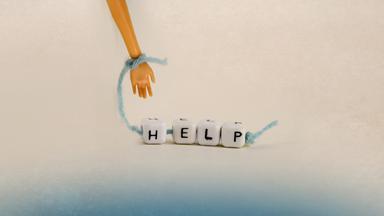 Kleine Hand hält ein Band mit Hölzkötzchen mit Aufschrift "Help"