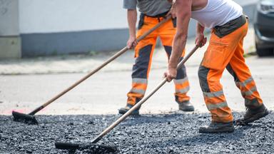 Bauarbeiter schieben heißen Aspahlt über die Sraße