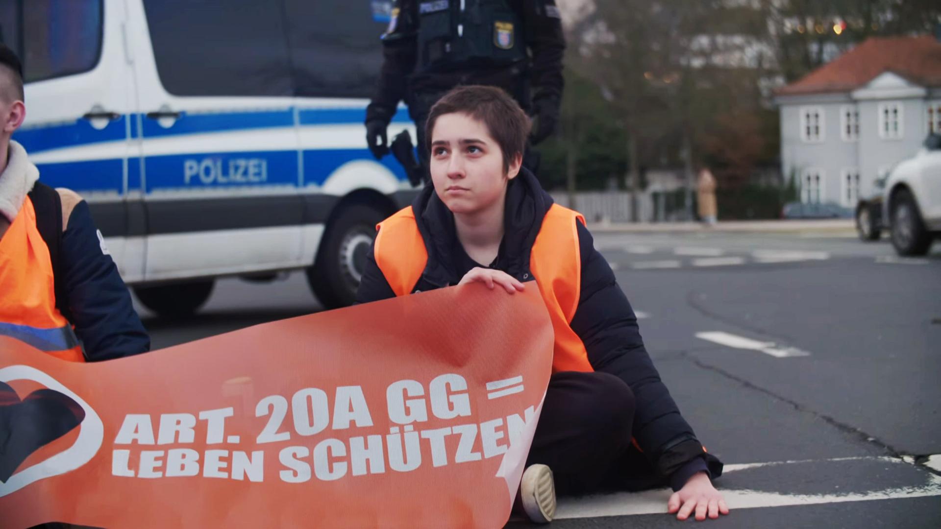 Junge Protestlerin sitzt auf der Straße