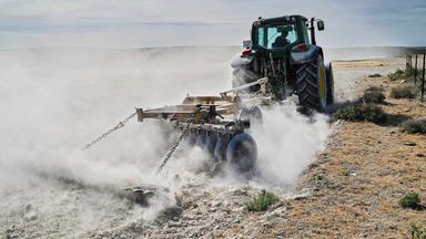 Traktor wirbelt Staub auf ausgetrocknetem Feld in Spanien auf.
