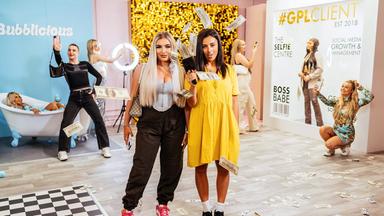 Zwei Frauen posieren vor der Kamera, eine hält ein Gerät in der Hand, aus dem Geldscheine fliegen. Im Hintergrund befinden sich fünf weitere Personen.