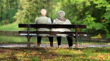 Zwei Rentner sitzen auf einer Bank und schauen ins Grüne