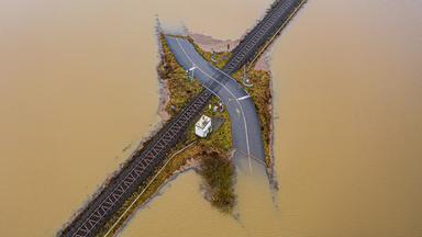 Überflutete Landschaft, aus der nur noch ein Bahndamm und Bahnübergang herausragt.