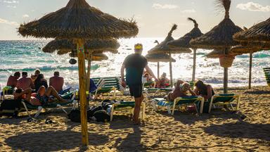 Ein Sandstrand mit Sonnenschirmen und Urlaubern mit Blick auf das Meer