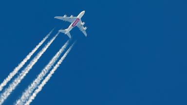 Flugzeug mit Kondensstreifen am blauen Himmel
