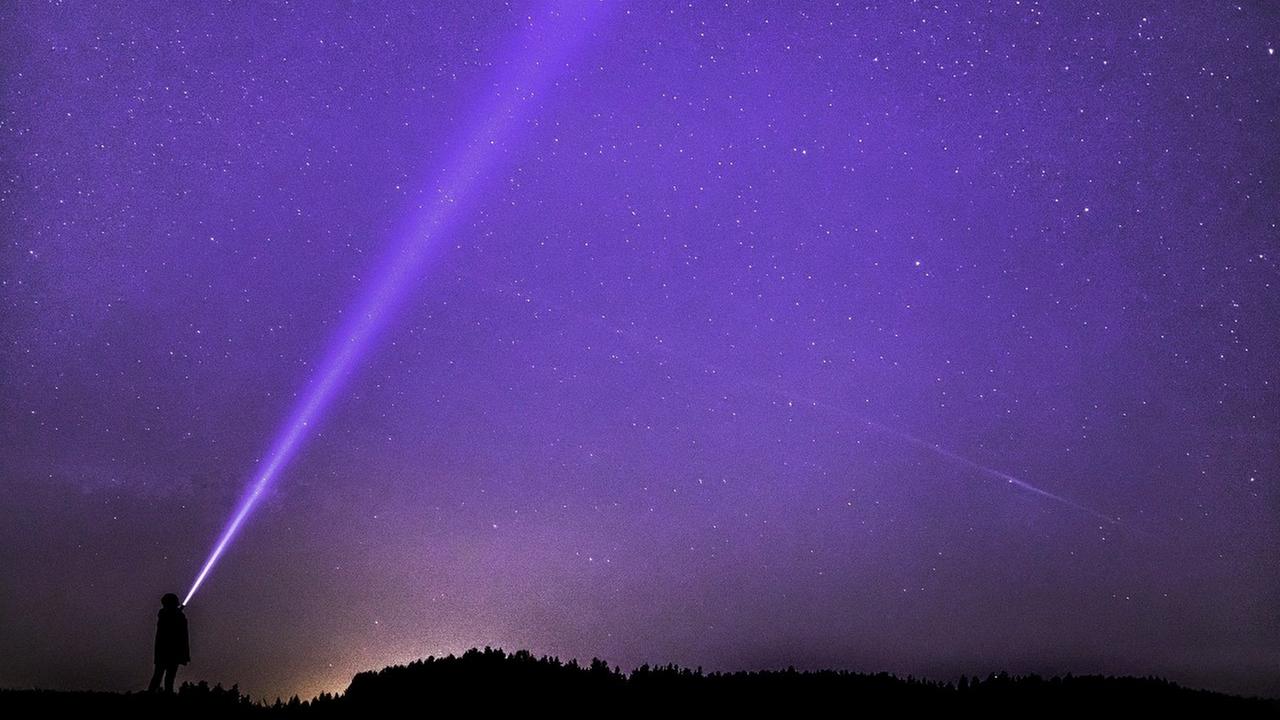 Mensch sucht mit einer Taschennlampe den Himmel nach außeriridschem Leben ab