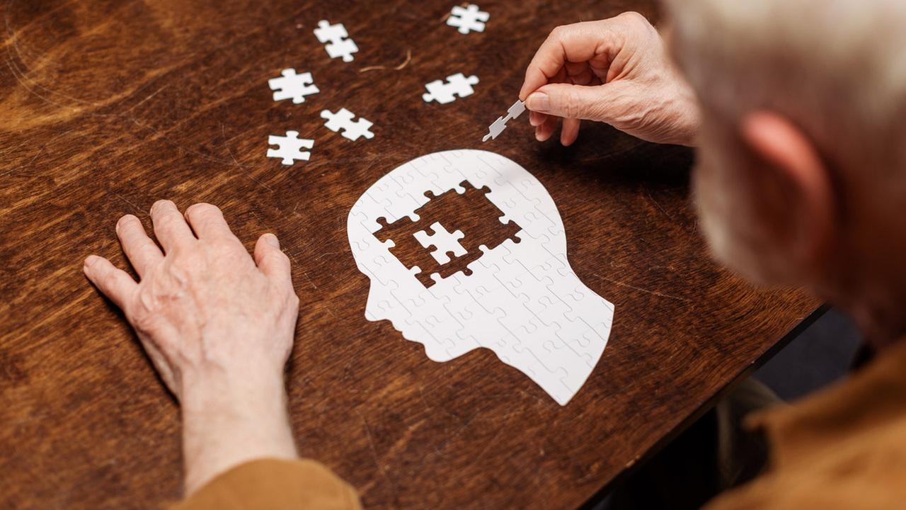 Die Ansicht eines alten Mannes, der ein Puzzle eines Kopfes zusammensetzt.