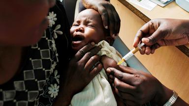 Ein weinendes Baby wird festgehalten und bekommt eine Spritze