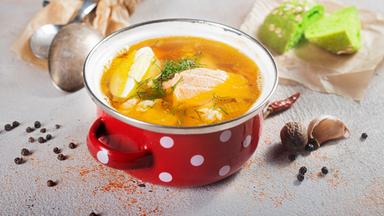 Im Zentrum ein roter Emaile-Kochtopf mit weissen Punkten mit einer Brühe und Fleischeinlage