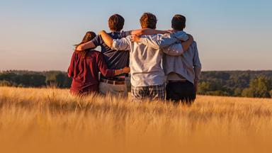 Gruppe junger Menschen. Sitzend auf einer Wiese, von hinten zu sehen