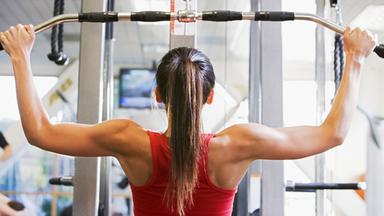 Frau im Fitnessstudio trainiert den Oberkörper, zu sehen von hinten