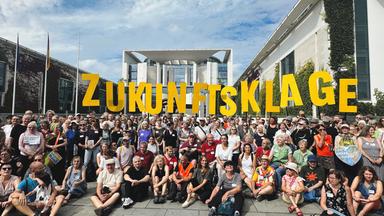 Menschen mit Schildern mit der Aufschrift ZUkunftsklage