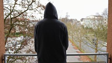 Junge Frau steht auf einem Balkon, zu sehen von hinten