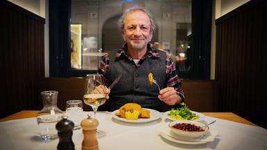 Ein Mann an einem gedeckten Essstisch lächelt in die Kamera.