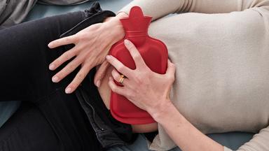 Frau hält sich eine Wämflasche auf den Bauch