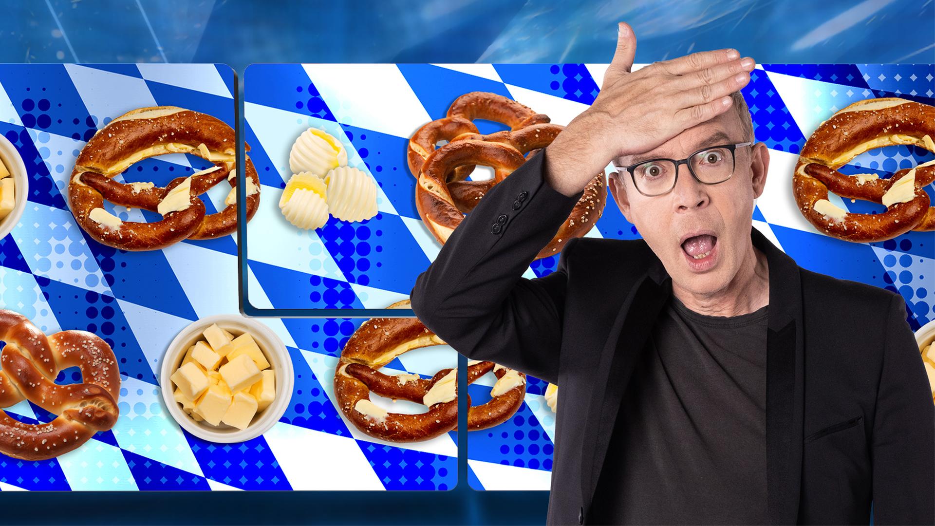 Der Moderator klatscht sich entsetzt die Hand vor die Stirn. Er steht vor einer Videowand, auf der Brezen und Butter zu sehen sind.