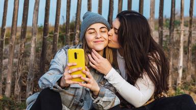 Ein Mädchen küsst ein anderes Mädchen auf die Wange, sie machen dabei ein Foto.