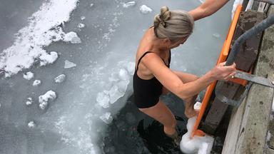 Eine Frau in einem Badeanzug steigt eine Leiter hinunter in einen teils zugefrorenen See